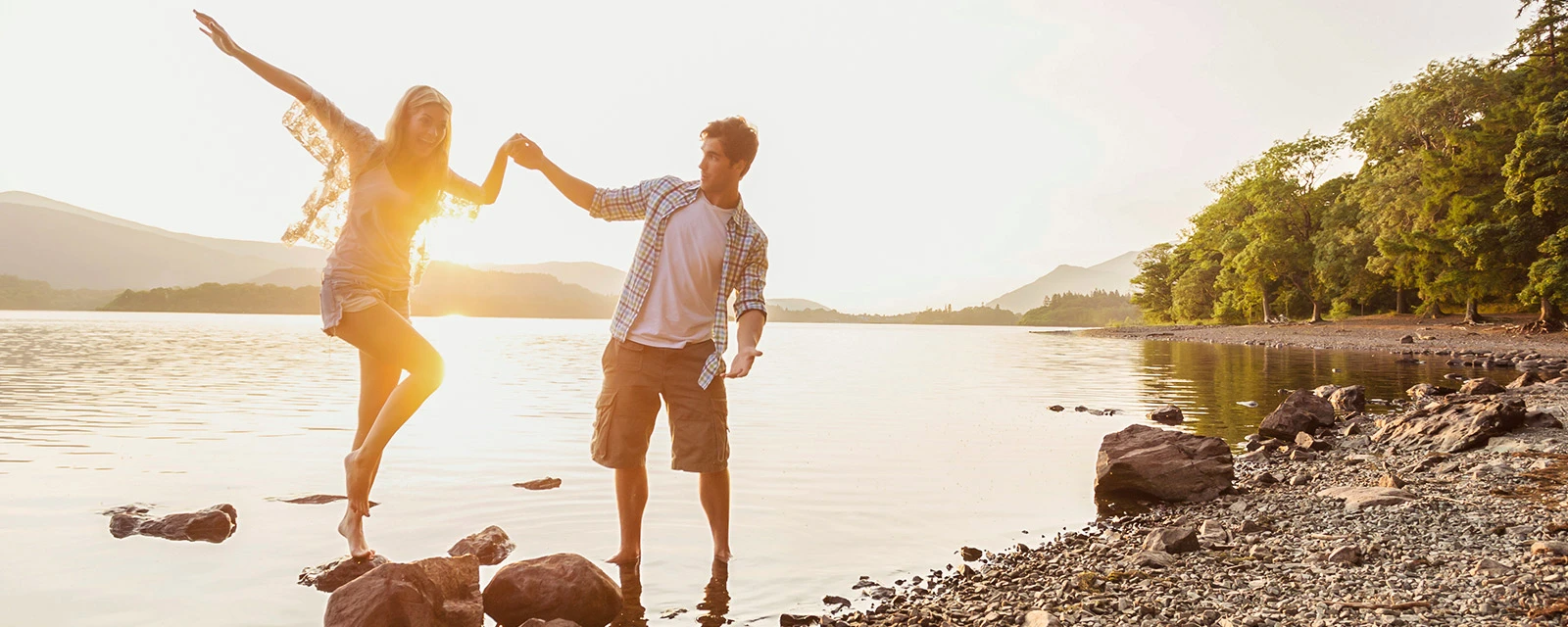 Ein Paar geht Hand in Hand bei Sonnenuntergang an einem Seeufer entlang