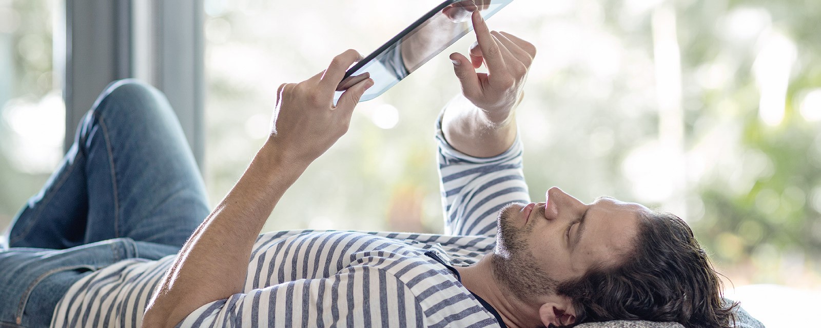 Ein junger Mann liet auf dem Sofa und hat sein Tablet in der Hand. Ein junger Mann liet auf dem Sofa und hat sein Tablet in der Hand.