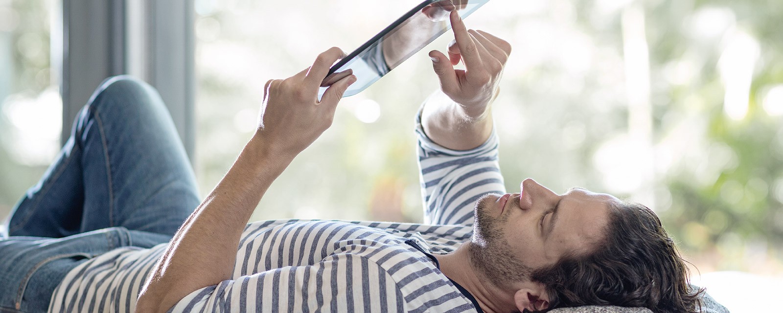 Ein junger Mann liet auf dem Sofa und hat sein Tablet in der Hand.