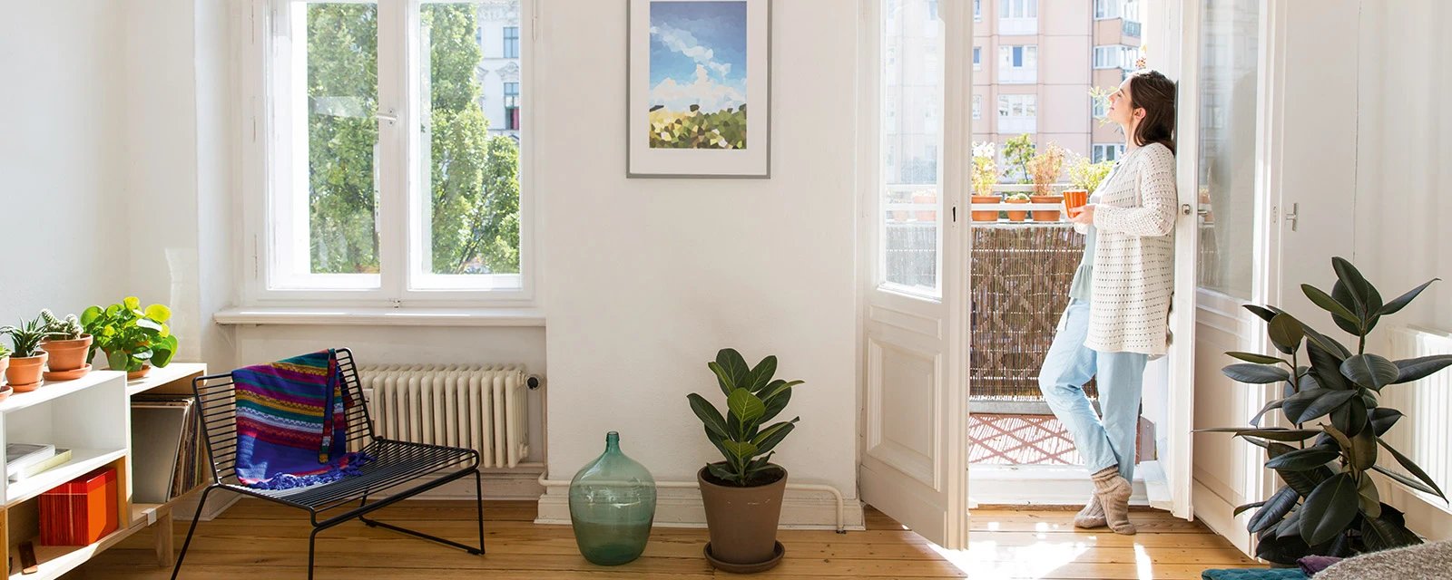 Frau steht in einer modernen Wohnung und schaut aus der Balkontür in die Sonne.