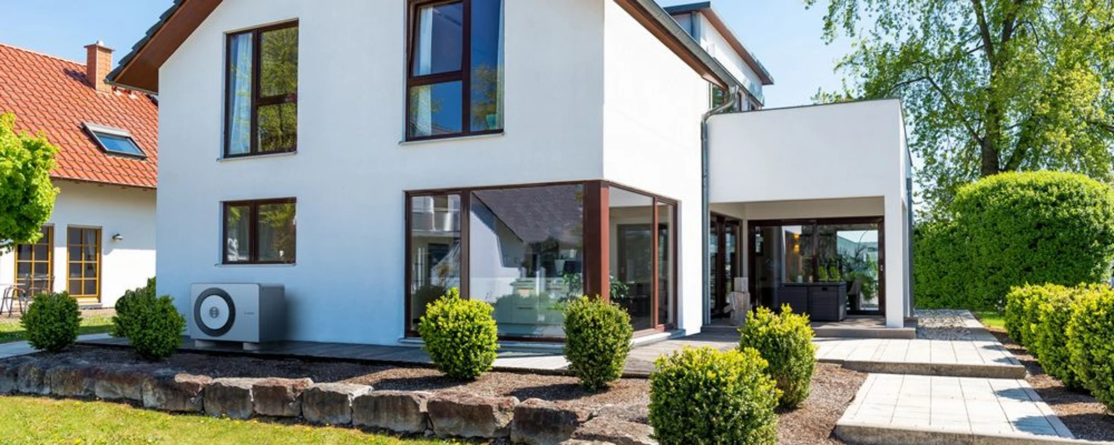 Die Wärmepumpe 5800i AW von Bosch steht an einer Hauswand eines modernen Hauses mit Vorgarten.