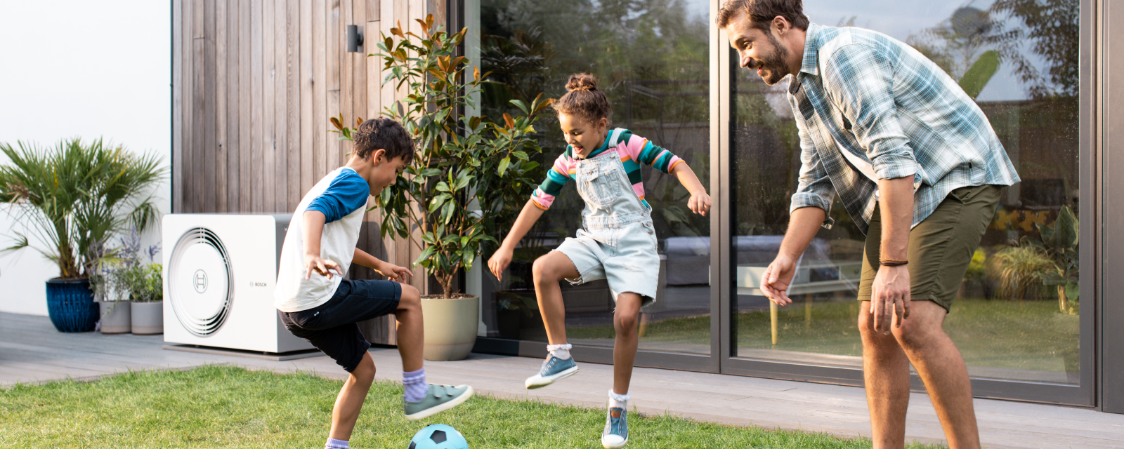 Hintergrund: Bosch Wärmepumpe Compress 5800, Vordergrund:Kinder mit Vater spielend im Garten Hintergrund: Bosch Wärmepumpe Compress 5800, Vordergrund:Kinder mit Vater spielend im Garten