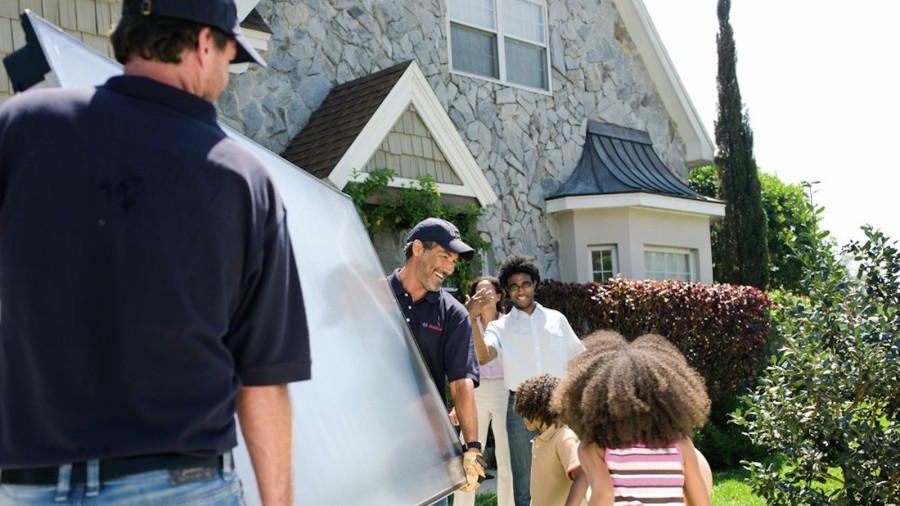 Zwei Fachleute von Bosch installieren Solarpanels für die Kombination mit einer Wärmepumpe und werden dabei von Kindern beobachtet. Zwei Fachleute von Bosch installieren Solarpanels für die Kombination mit einer Wärmepumpe und werden dabei von Kindern beobachtet.