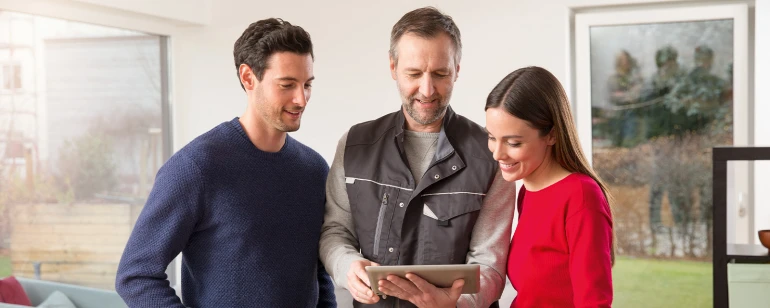 Paar lässt sich von Heizungsmonteur auf einem Tablet die Erdwärmepumpe zeigen