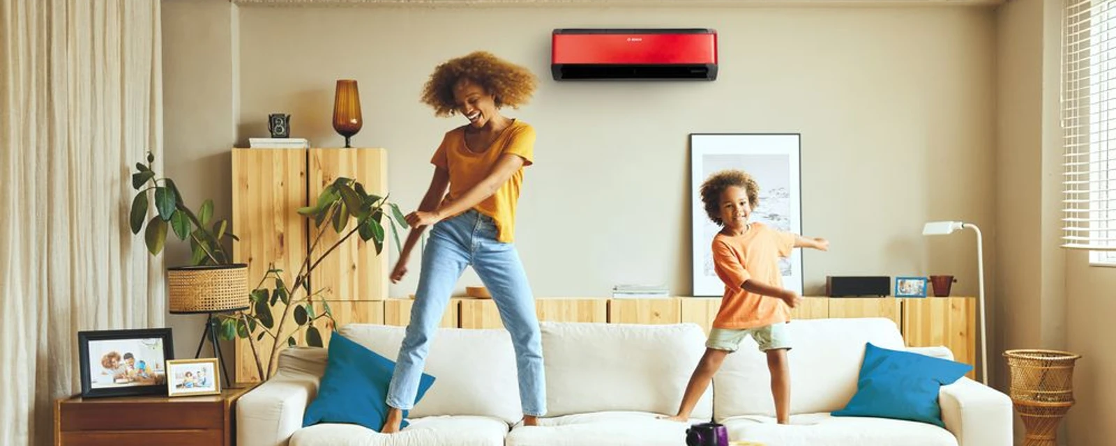 Woman and children dancing on a couch in front of an air conditioning.