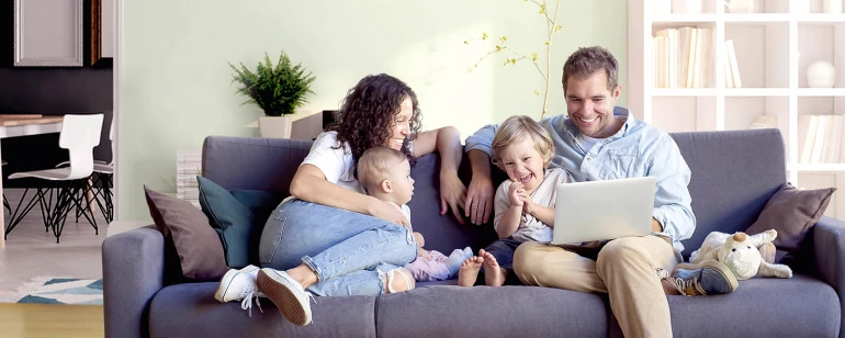 Een gezin zit samen op een bank in de woonkamer, die op een comfortabele temperatuur wordt gehouden door een Bosch airconditioner.