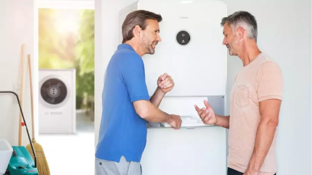 Two men standing in front of an air-to-water heat pump and chatting