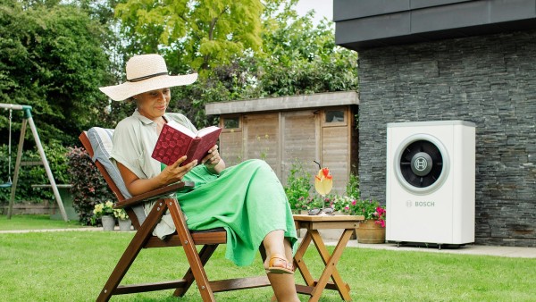 Een vrouw zit in haar tuin een boek te lezen, ongestoord door de stille warmtepomp achter haar.