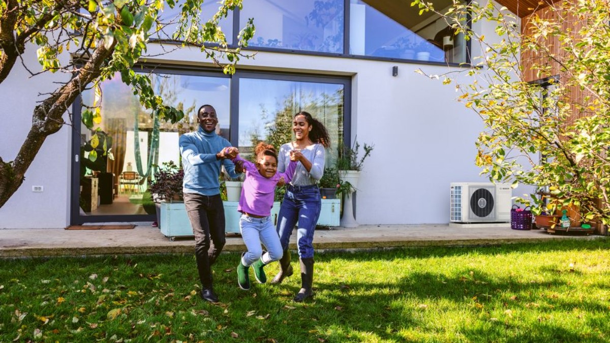 Familie die aan het spelen is met op de achtergrond een buitenunit van de hybride warmtepomp 3400 Familie die aan het spelen is met op de achtergrond een buitenunit van de hybride warmtepomp 3400