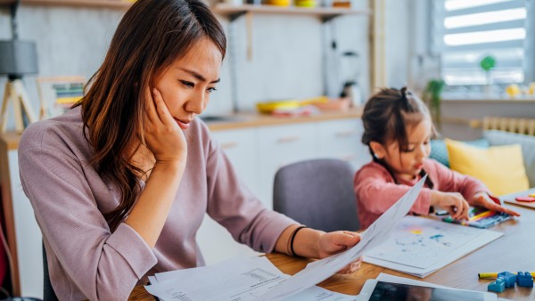 mother paying bills at kitchen table while her child plays