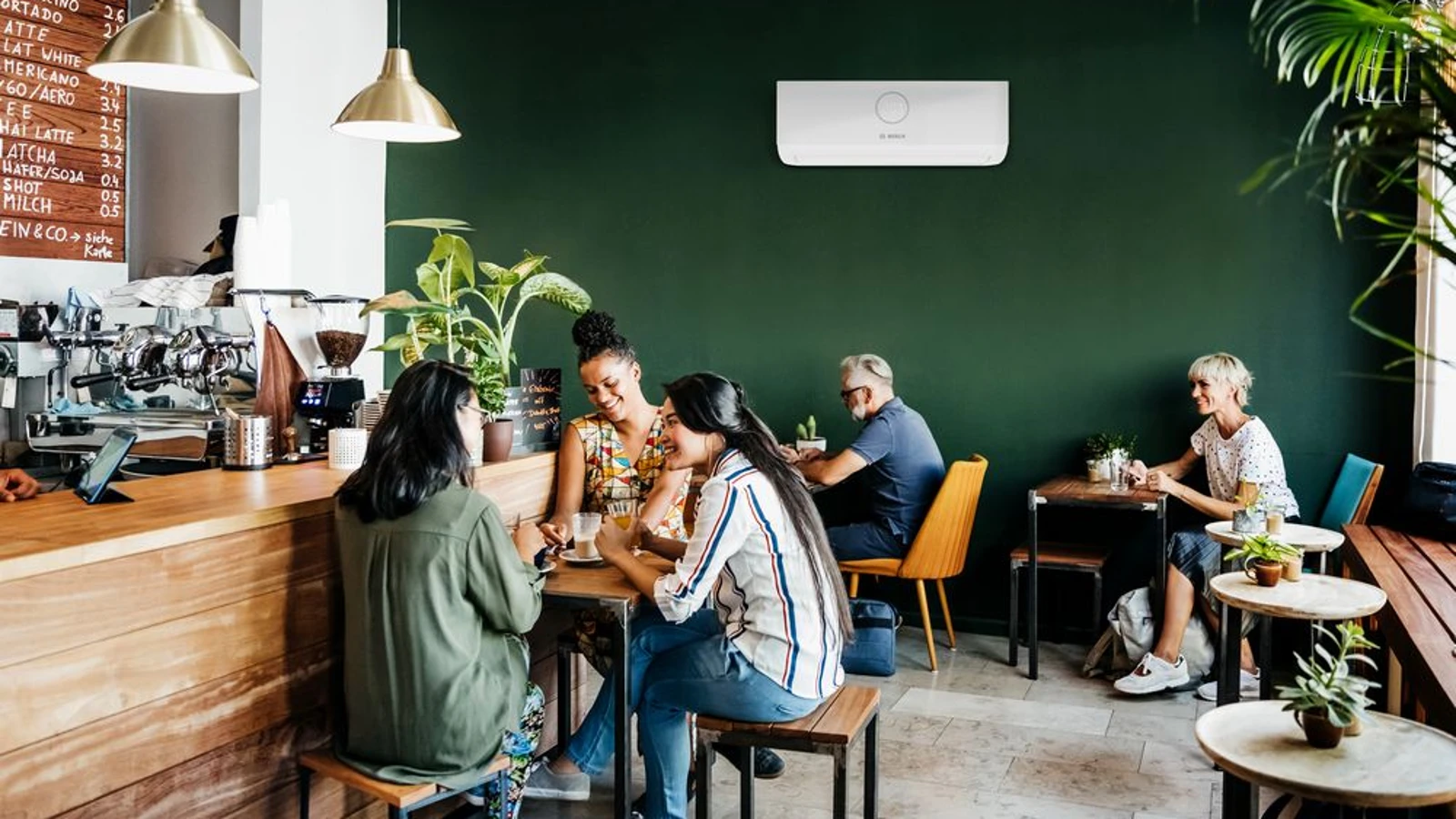 Eine Klimaanlage von Bosch an der Wand in einem Café voller Menschen.