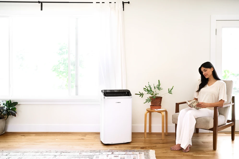 Das mobile Klimagerät Cool 5000 von Bosch in einem Wohnzimmer stehend, daneben eine Frau auf einem Sessel, welche gerade etwas liest.