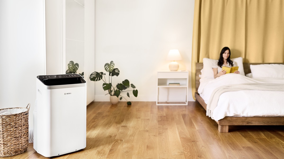 Eine Frau liegt im Bett, während neben ihr das mobile Klimagerät Cool 5000 von Bosch steht.