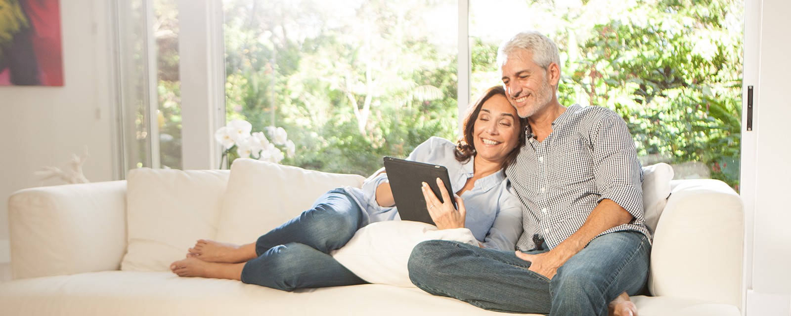 EIn Paar sitzt auf der Couch und hat ein Tablet in der Hand.