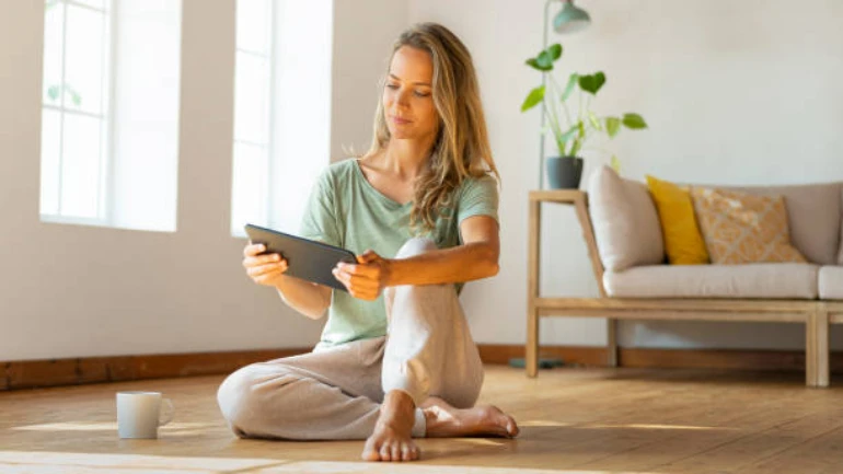 Eine Frau sitzt auf dem Boden in ihrer Wohnung und liest den Bosch HC Newsletter auf ihrem Tablet.