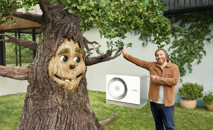 Ein Baum mit einem lächelnden Gesicht gibt einem Mann ein High-Five - während im Hintergrund eine Wärmepumpe zu erkennen ist.