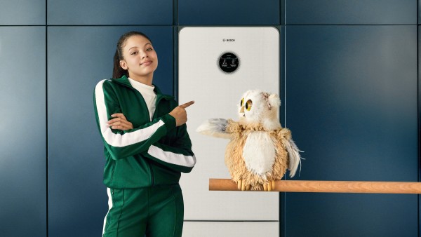 Eine Frau in einem Trainingsanzug steht mit einer Eule vor der Wärmepumpe Compress 7800 LW von Bosch in einer Küche..