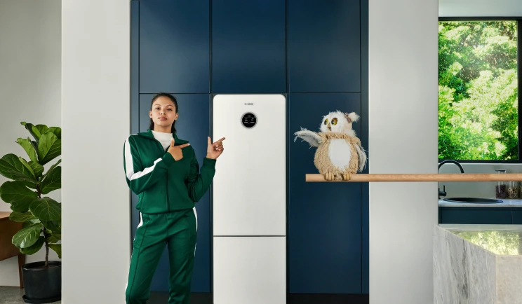 Frau in einem Trainingsanzug steht mit einer Eule vor Wärmepumpe Compress 7800 LW von Bosch in einer Küche.