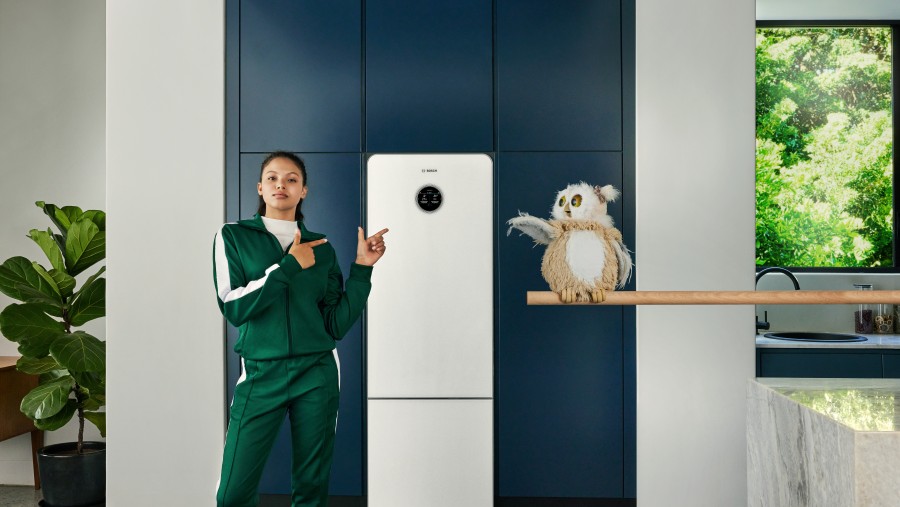 Frau in einem Trainingsanzug steht mit einer Eule vor Wärmepumpe Compress 7800 LW von Bosch in einer Küche.