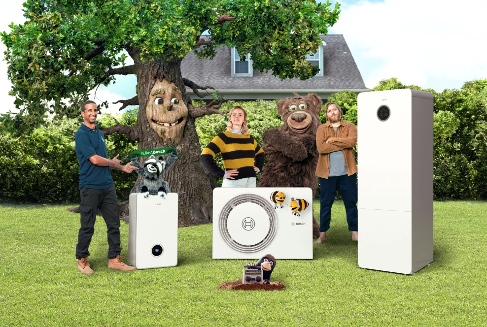 Zwei Männer, eine Frau, eine Biene, ein Waschbär, ein Bär, ein Maulwurf sowie ein Baum stehen in einem Garten. Davor stehen drei verschiedene Heizgeräte von Bosch.