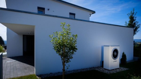 Wärmepumpe steht an Hauswand neben einem Baum