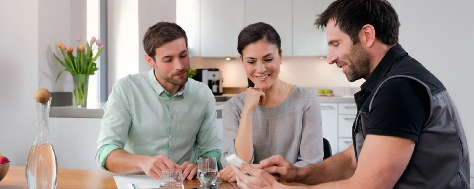 Ein Paar sitzt mit einem Installateur an einem Küchentisch und unterhält sich.