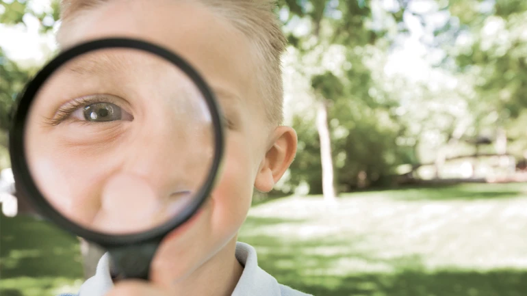 Kleiner Junge schaut durch eine Lupe und steht im Garten