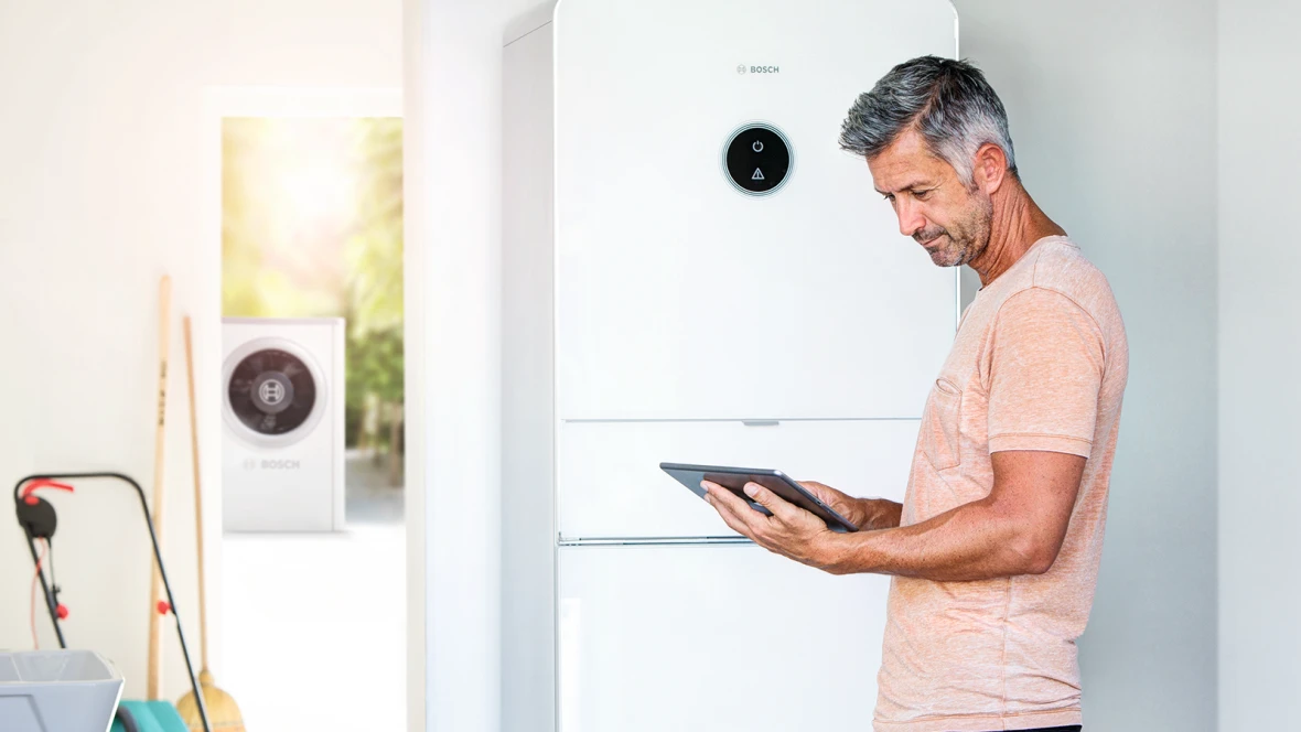 Mann steht neben Bosch Compress 7000i AW Wärmepumpe und bedient ein Tablet