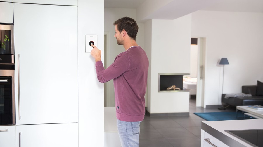 Ein Mann bedient den Bosch Regler Easy Control, der an der Wohnzimmerwand montiert ist. Ein Mann bedient den Bosch Regler Easy Control, der an der Wohnzimmerwand montiert ist.