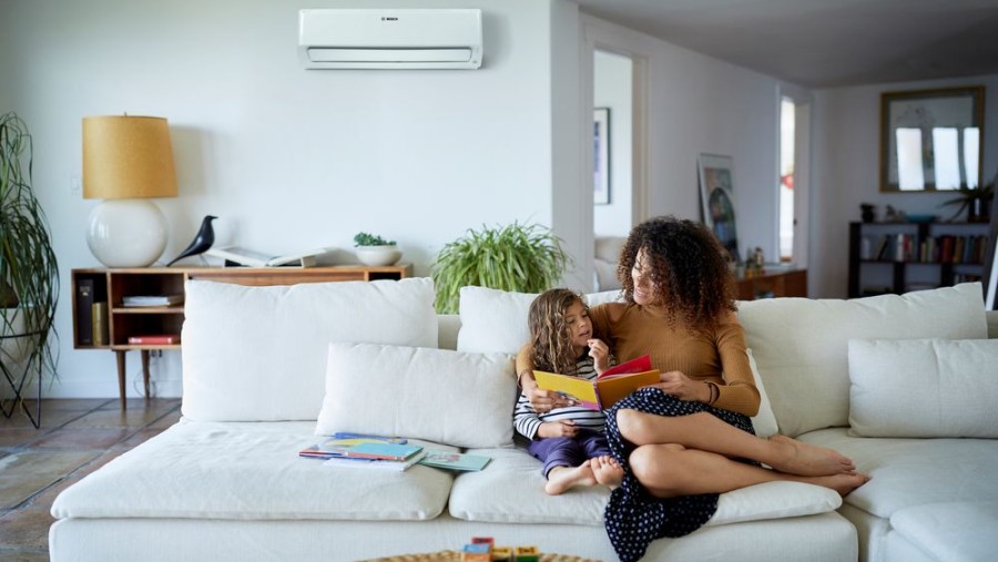 Climate Class 6000i in der Wohnung an der Wand hinter dem Sofa montiert, auf dem Sofa sitzt eine Mutter mit einem Kind.