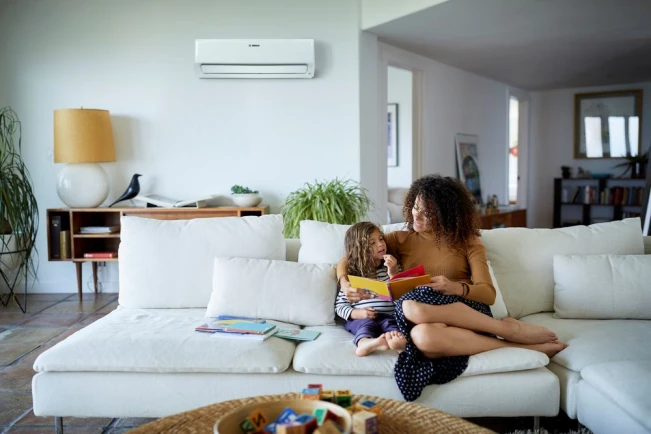 Climate Class 6000i in der Wohnung an der Wand hinter dem Sofa montiert, auf dem Sofa sitzt eine Mutter mit einem Kind.
