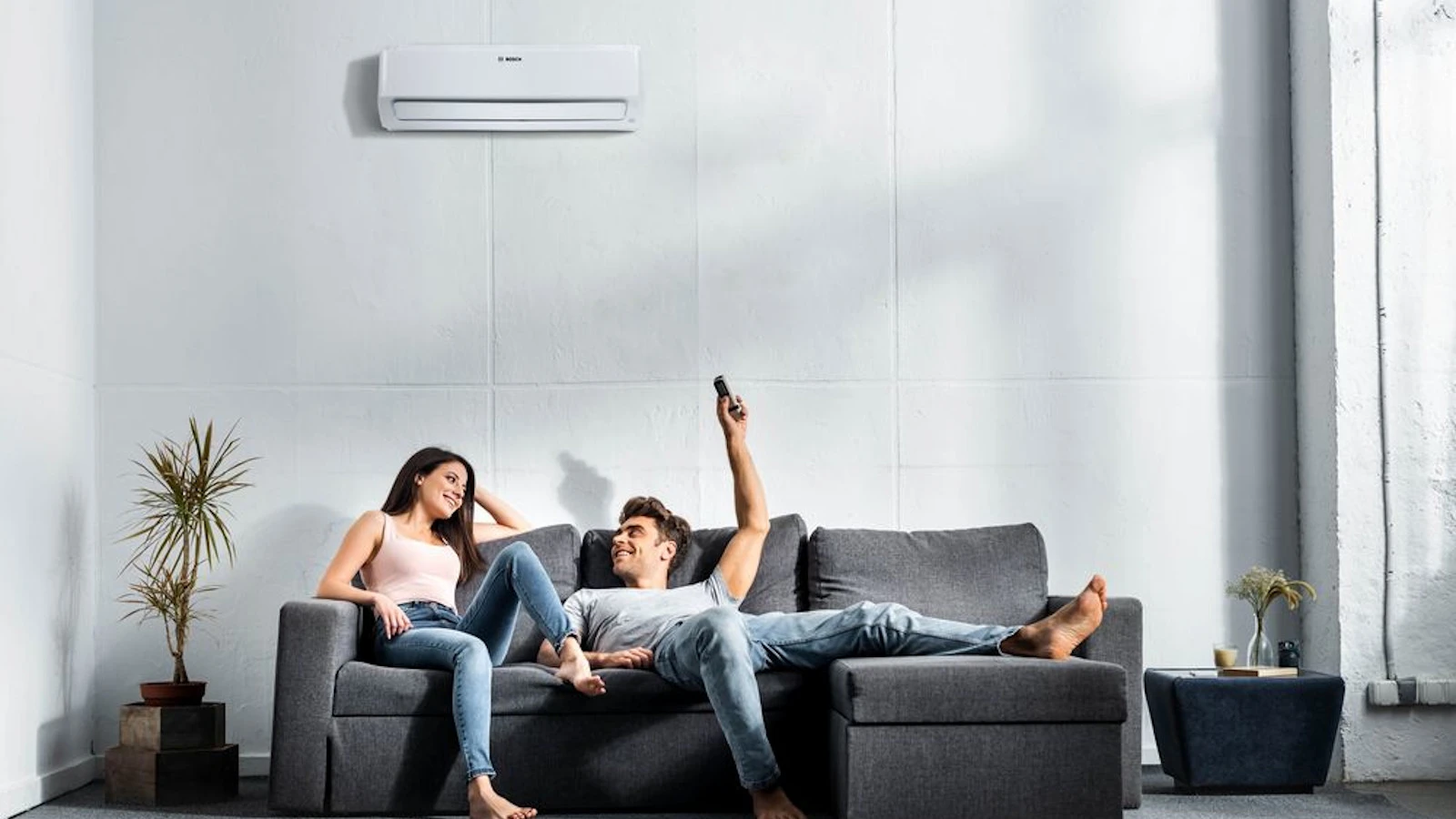 Ein Paar sitzt auf einem Sofa, während eine Person die Fernbedienung auf die Wandklimaanlage richtet. Wenn die Klimaanlage nicht mehr kühlt, liegt es oft nicht an einem Defekt, sondern an einer falschen Einstellung.