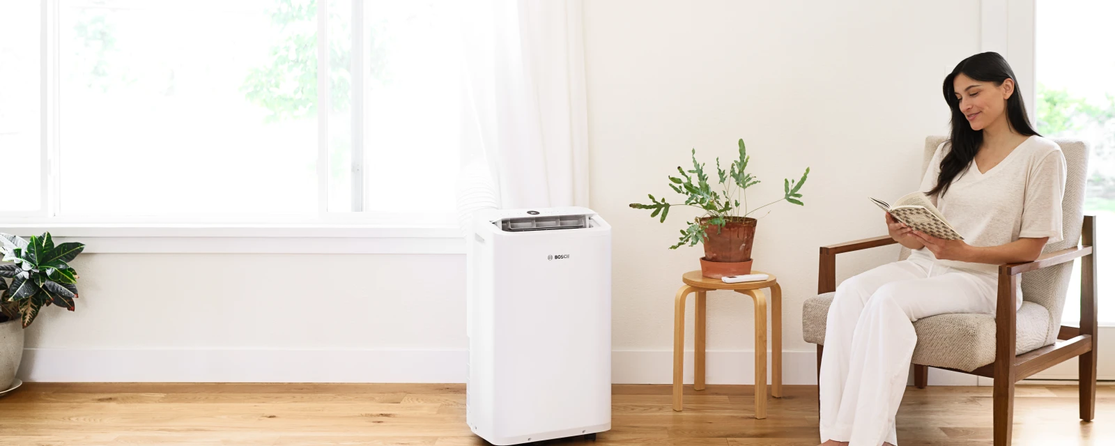 Frau sitzt in einem Stuhl und liest Buch, während sie die kühle Luft der mobilen Klimaanlage von Bosch genießt.
