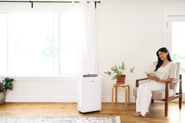 Frau auf einem Stuhl neben ihr steht eine mobile Klimaanlage