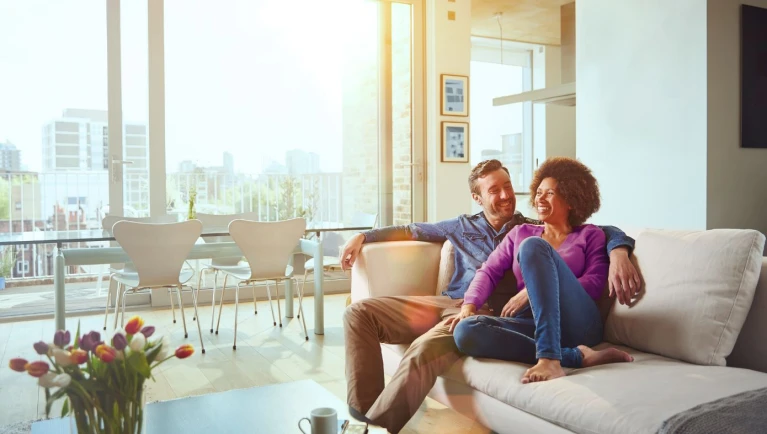 Pärchen sitzt im Wohnbereich auf dem Sofa und genießt das Tageslicht und die Sonnenwärme.