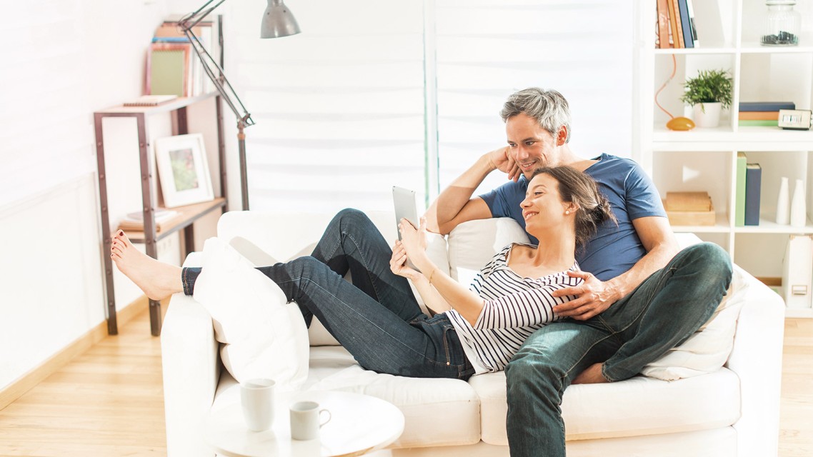 Pärchen sitzt auf dem Sofa und schaut auf ein Tablett