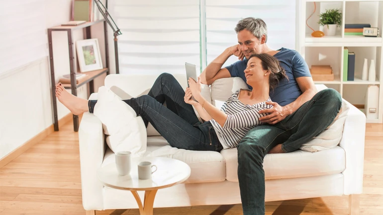 Ein Paar sitzt auf einem Sofa und sieht gemeinsam auf ein Tablet.