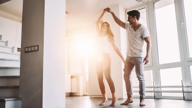 Ein Paar tanzt in der Wohnung während die Sonne durch die Fenster scheint