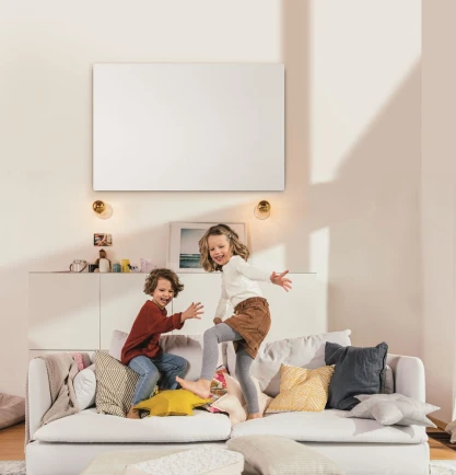 Kinder spielen auf dem Sofa, darüber hängt eine Infrarotheizung an der Wand