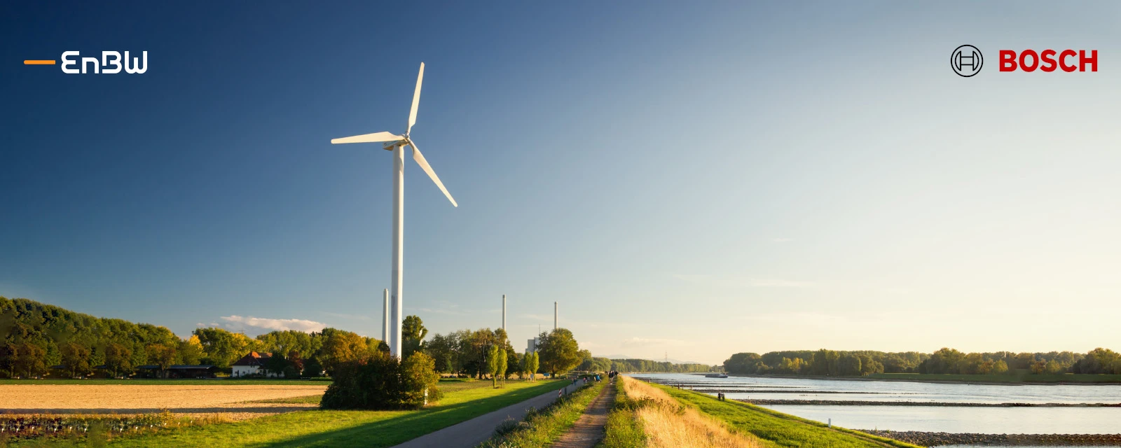 Ein Windrad steht in der Natur zwischen Ackerfeldern, parallel verläuft eine Straße.