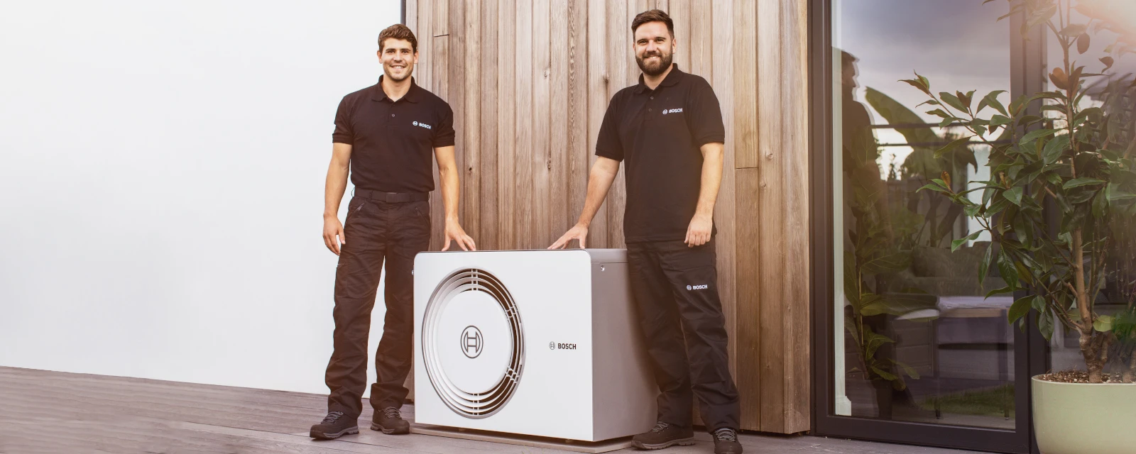 Zwei Bosch Installateure stehen neben der Wärmepumpe Compress 5800i AW.