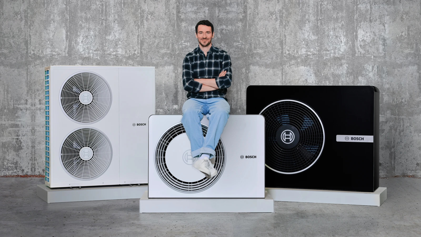 Felix Neureuther sitzt auf einer Wärmepumpe von Bosch. Daneben sind weitere Wärmepumpen-Modelle zu sehen.
