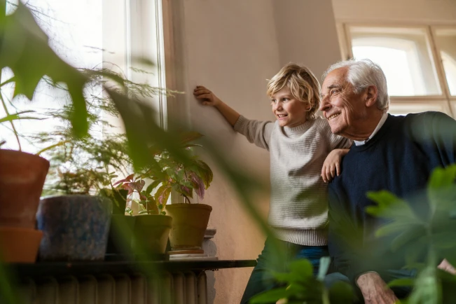 Opa und Enkelkind beobachten etwas vom Fenster aus in der Wohnung.