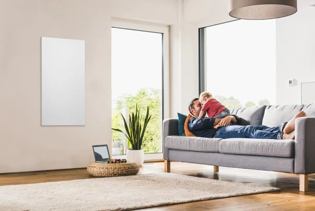 Vater und Tochter liegen auf der Couch, links neben ihnen hängt an der Wand die neue Infrarotheizung von Bosch