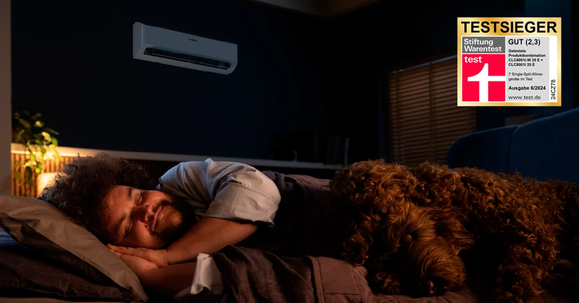 Ein Mann und sein Hund befinden sich im Schlafzimmer. Im Hintergrund ist die Bosch Climate Class 8000i zu sehen. Zudem ist das Testsieger Logo von Stiftung Warentest abgebildet.