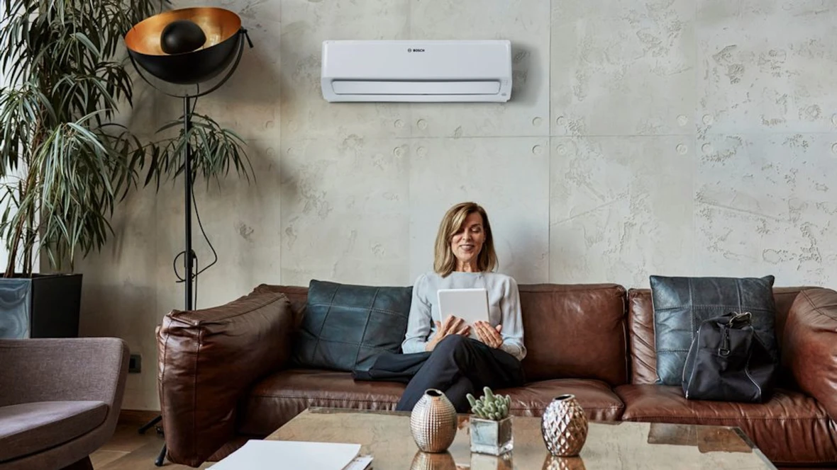 Frau sitzt auf dem Sofa und hat ein Tablet in der Hand, im Hintergrund hängt an der Wand die Bosch Climate Class 6000i