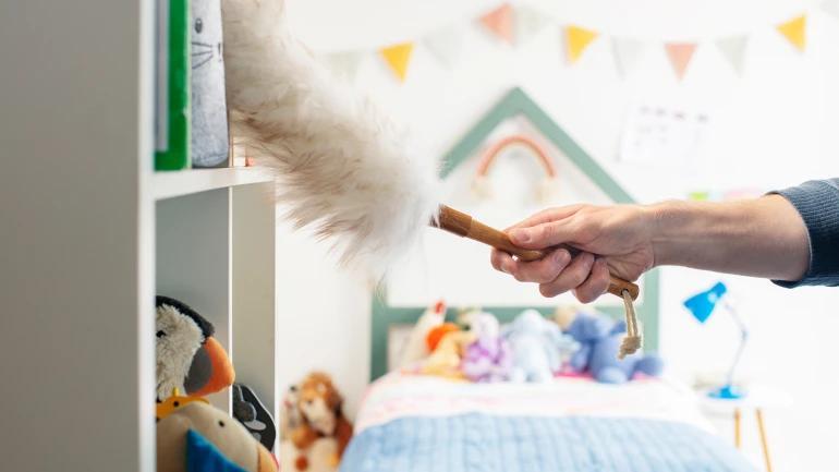 Eine Person wischt Staub aus den Regalen in einem Kinderzimmer.