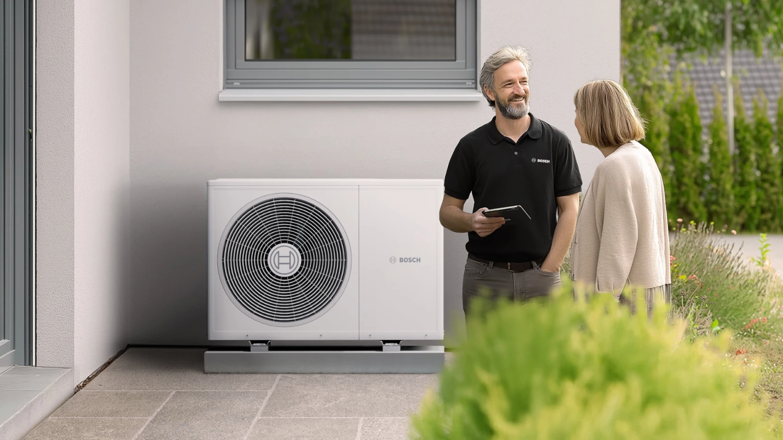 Bosch Fachmann informiert Kundin über Lebensdauer der Wärmepumpe vor Außengerät