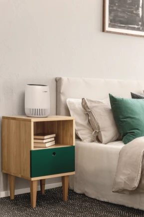 Neben einem Bett steht ein Luftreinigungsgerät von Bosch.