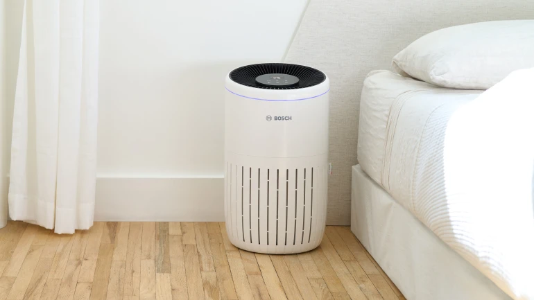 Ein Luftreiniger steht neben einem Bett.
